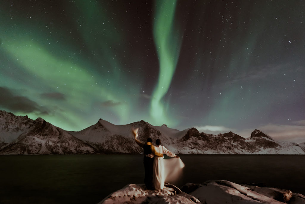 Un couple de mariés sous les aurores boréales dans un fjord en Norvège sur Senja. Mariage elopement sous les aurores boréales avec leur photographe Gaétane Glize.