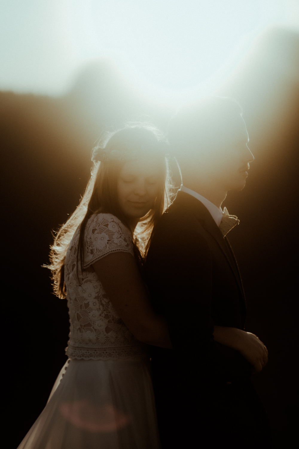 La mariée fait un câlin à son mari avec la belle lumière dorée du coucher du soleil et les montagnes en fond. Un moment doux capté par Gaétane Glize, photographe elopement Pyrénées.