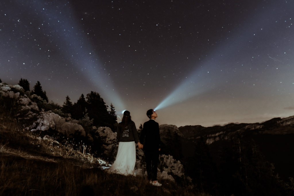 Un couple de mariés est en montagne de nuit avec leur lampe frontale. On voit les étoiles. Une astrophotographie de mariage réalisée par Gaétane Glize, photographe elopement Pyrénées.