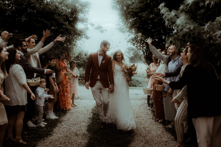 Les mariés marchent main dans la main sous une pluie de pétales séchés à la sortie de leur cérémonie de mariage dans les Landes.