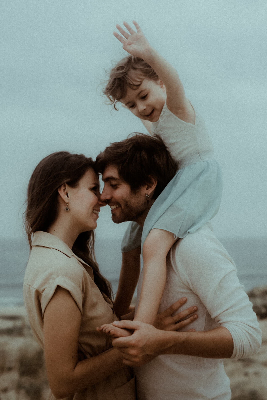 Une mère et un père s'embrassent avec leur fille sur les épaules. Un instant saisi pendant leur séance photo famille sur la plage de Labenne dans les Landes.