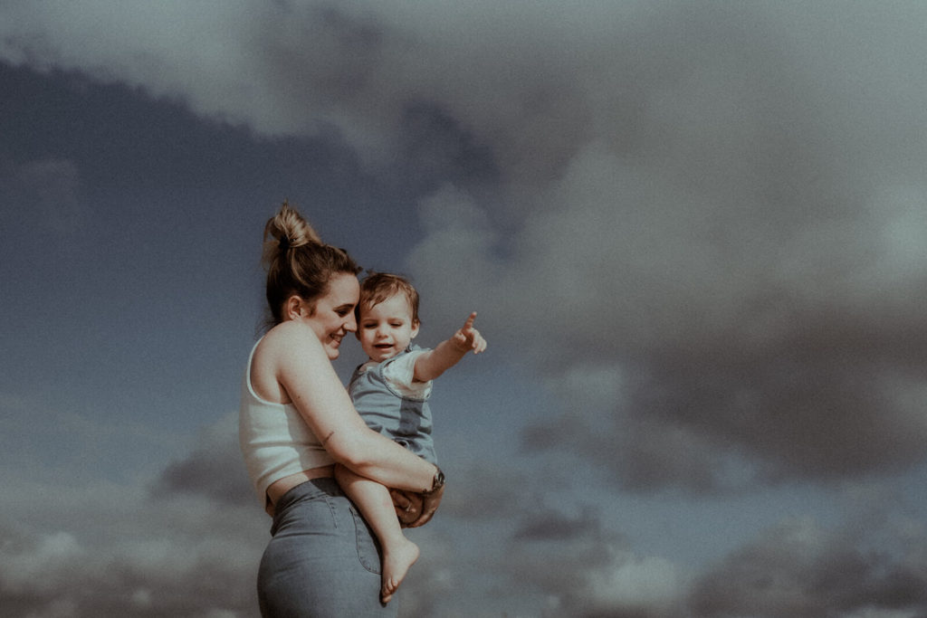 La maman porte sa fille dans les bras, le ciel est nuageux, le temps parfait pour une séance photo famille dans les Landes.