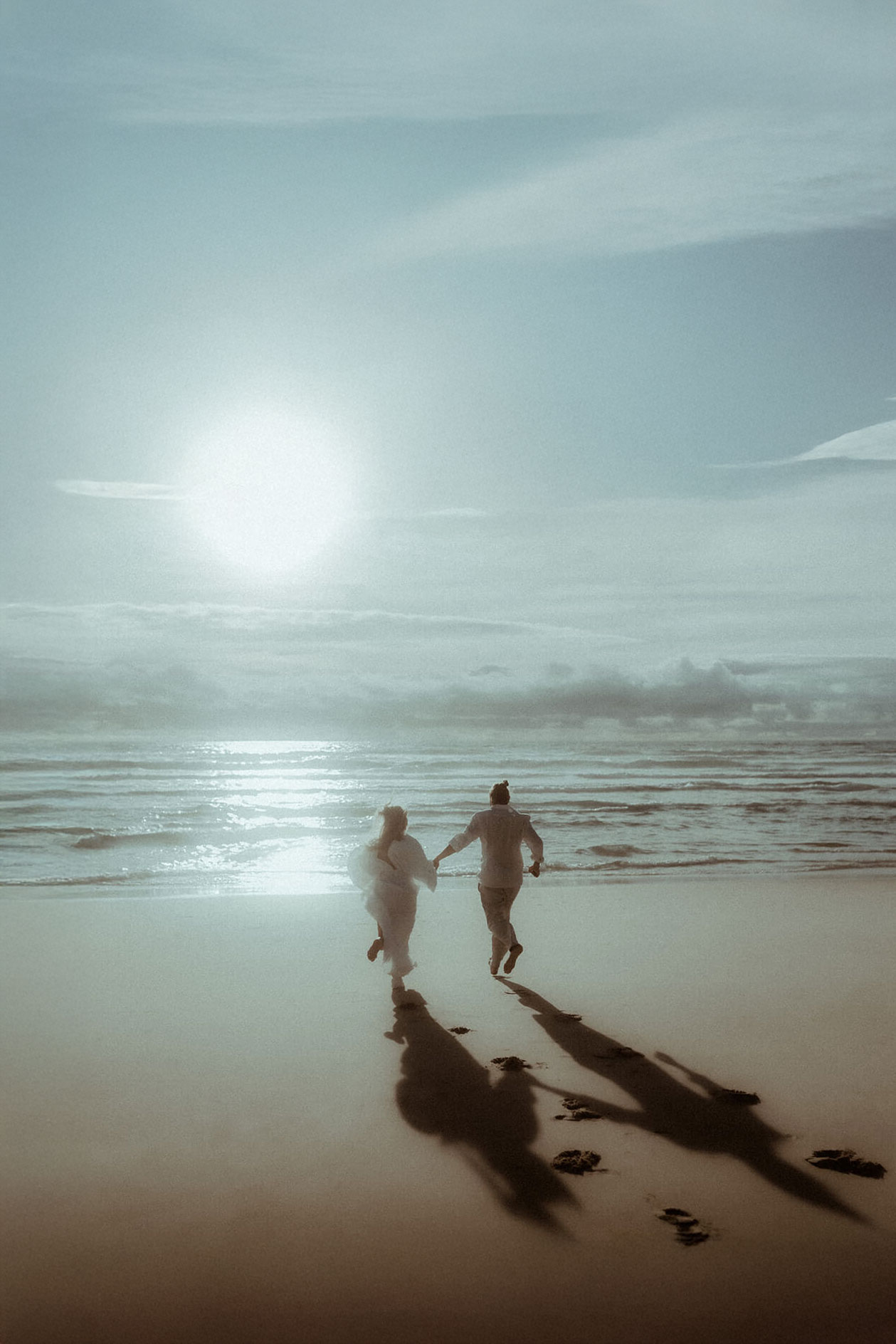 Un couple court main dans la main sur la plage en direction de l'océan et du coucher de soleil pendant leur séance photo de couple à Hossegor dans les Landes.