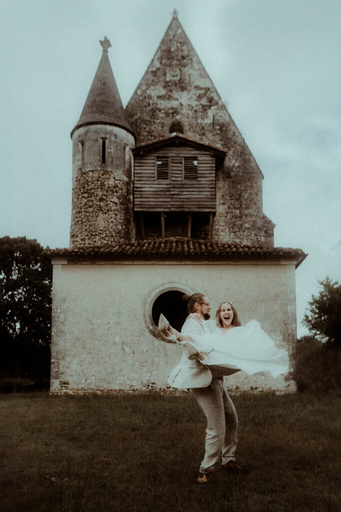 Le marié fait tournoyer sa femme. Le couple rit aux éclats devant la chapelle dans laquelle ils ont célébré leur mariage dans les Landes. Un moment fun capturé par la photographe de mariage Gaétane Glize pendant leur elopement.