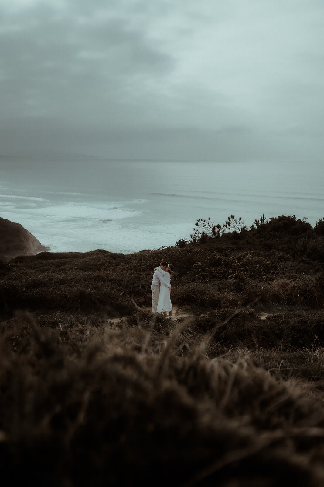 Un couple s'enlace sur la falaise de Biarritz avec l'océan et les montagnes en fond. Un moment capturé par Gaétane Glize, photographe couple pays basque, pendant leur séance photo fiançailles.