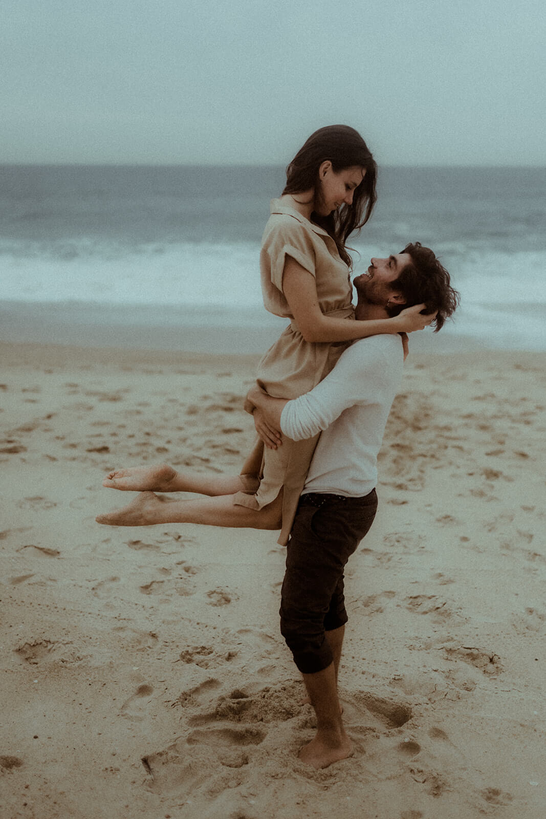 Un couple s'amuse sur la plage de Labenne pendant leur séance photo couple avec Gaétane Glize, photographe couple landes. L'homme porte la femme devant l'océan.