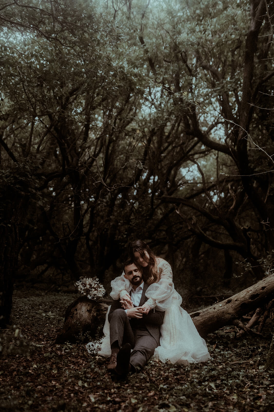 Un couple est assis dans la forêt des landes, ils s'enlacent tendrement sur un tronc d'arbre. Un moment de douceur pendant leur séance photo de couple à Seignosse.