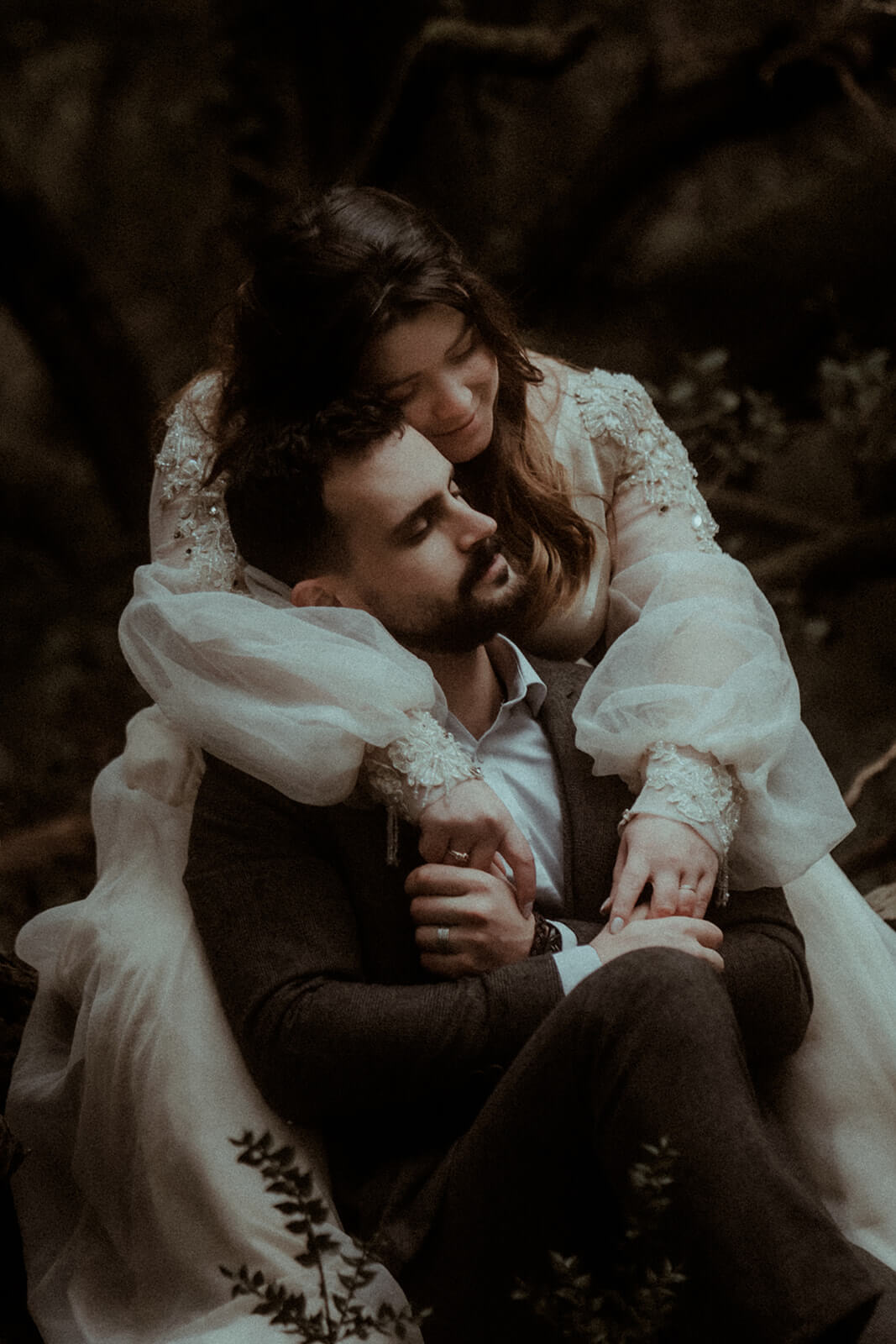 Un couple de mariés sont assis l'un dans les bras de l'autre dans la forêt. La mariée étreint son mari et leurs visages se touchent. Un moment très doux et tendre capturé par Gaétane Glize, photographe mariage Landes.