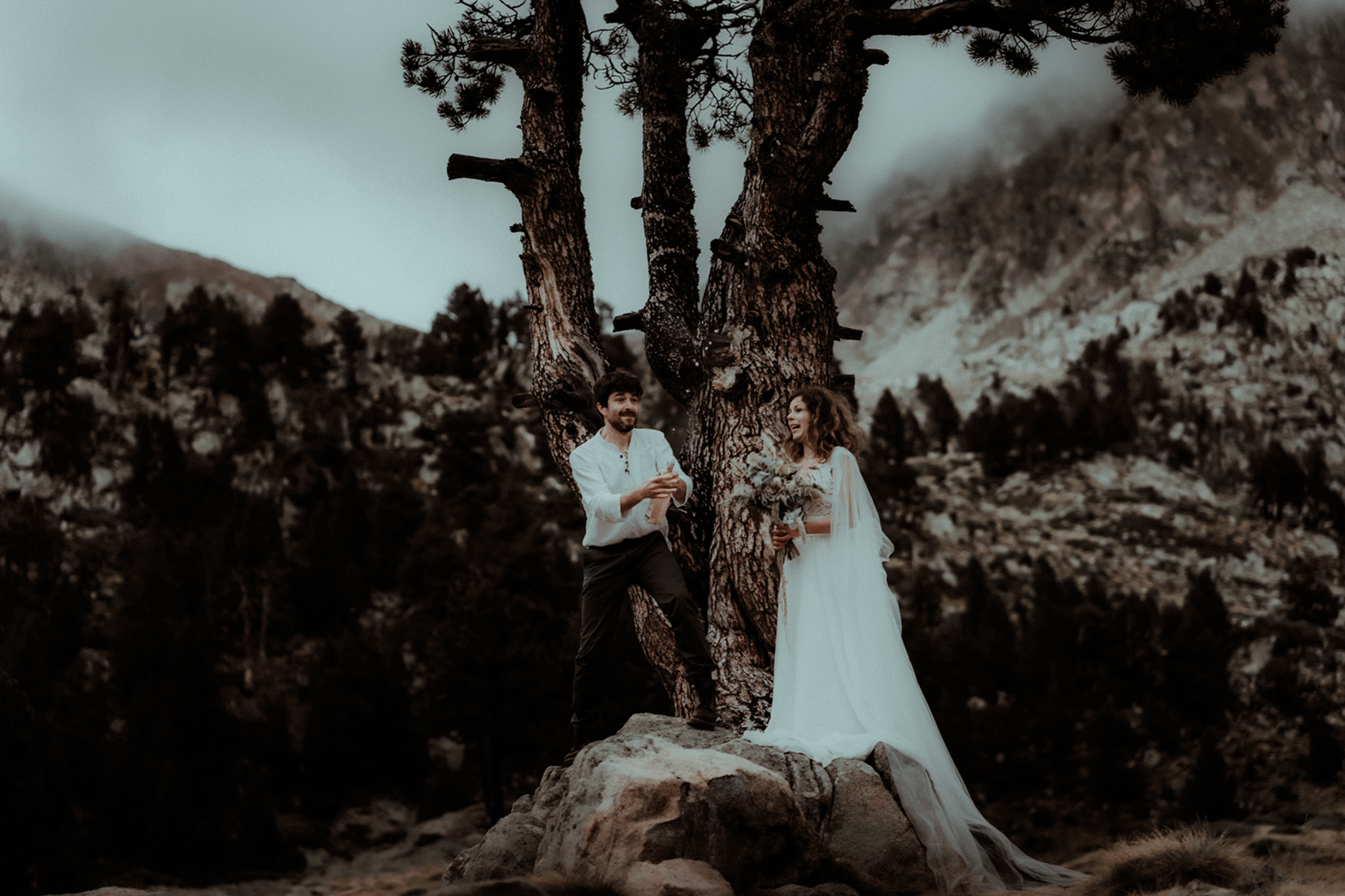 Le couple de mariés célèbrent leur mariage en secouant une bouteille de champagne. On voit les montagnes et les sapins en fond. Un moment capté par Gaétane Glize, photographe elopement Pyrénées.