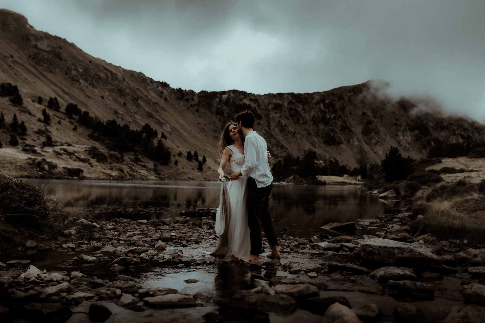 Un couple danse au bord d'un lac de montagne dans les Pyrénées. Une première danse capturée par Gaétane Glize, photographe elopement Pyrénées.